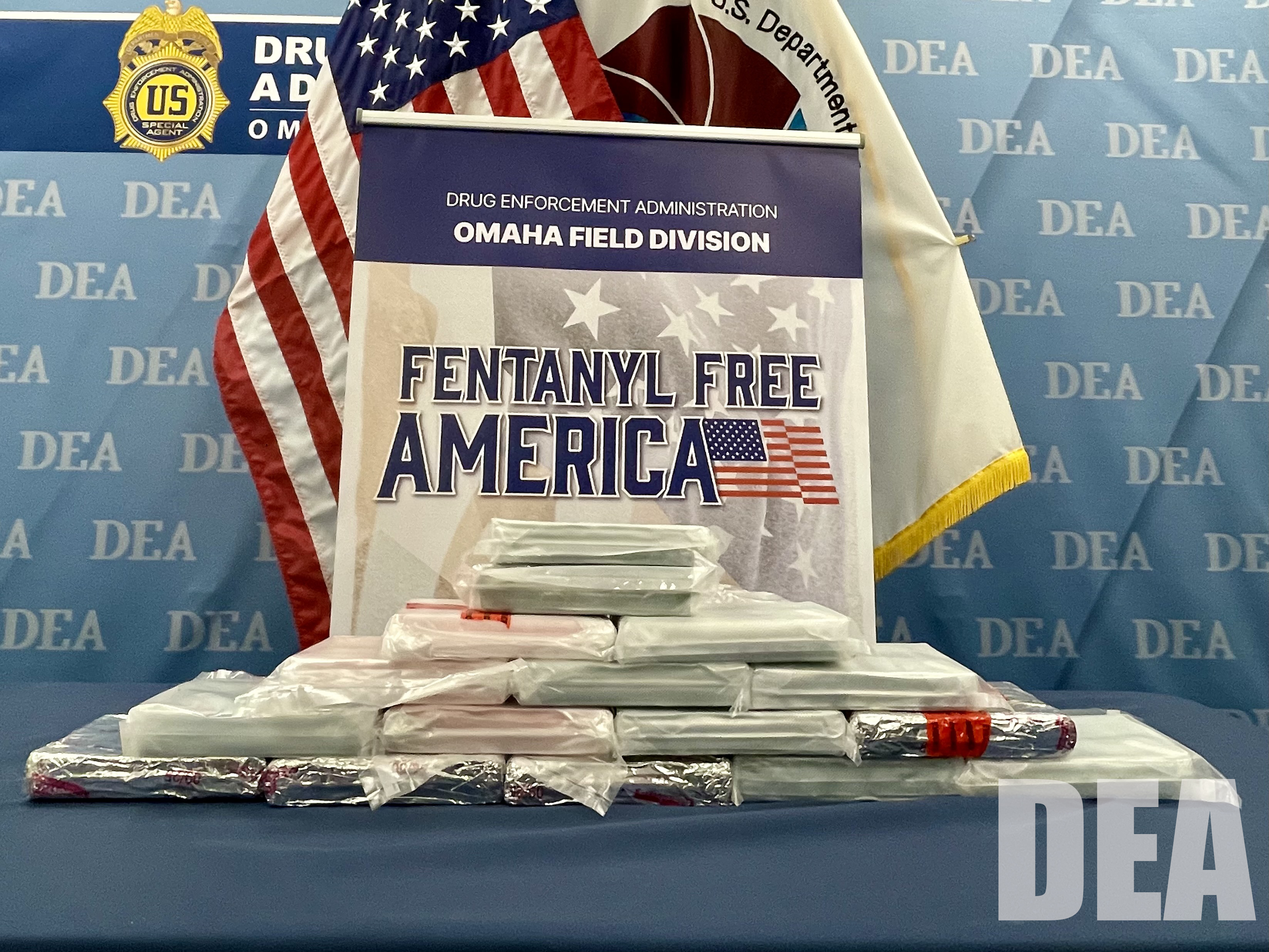A table holds several bricks of fentanyl with the DEA Omaha Field Division banner reading Fentanyl Free America sitting behind.
