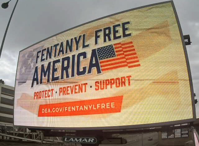 An American flag with the words Fentanyl Free America is displayed on a billboard.