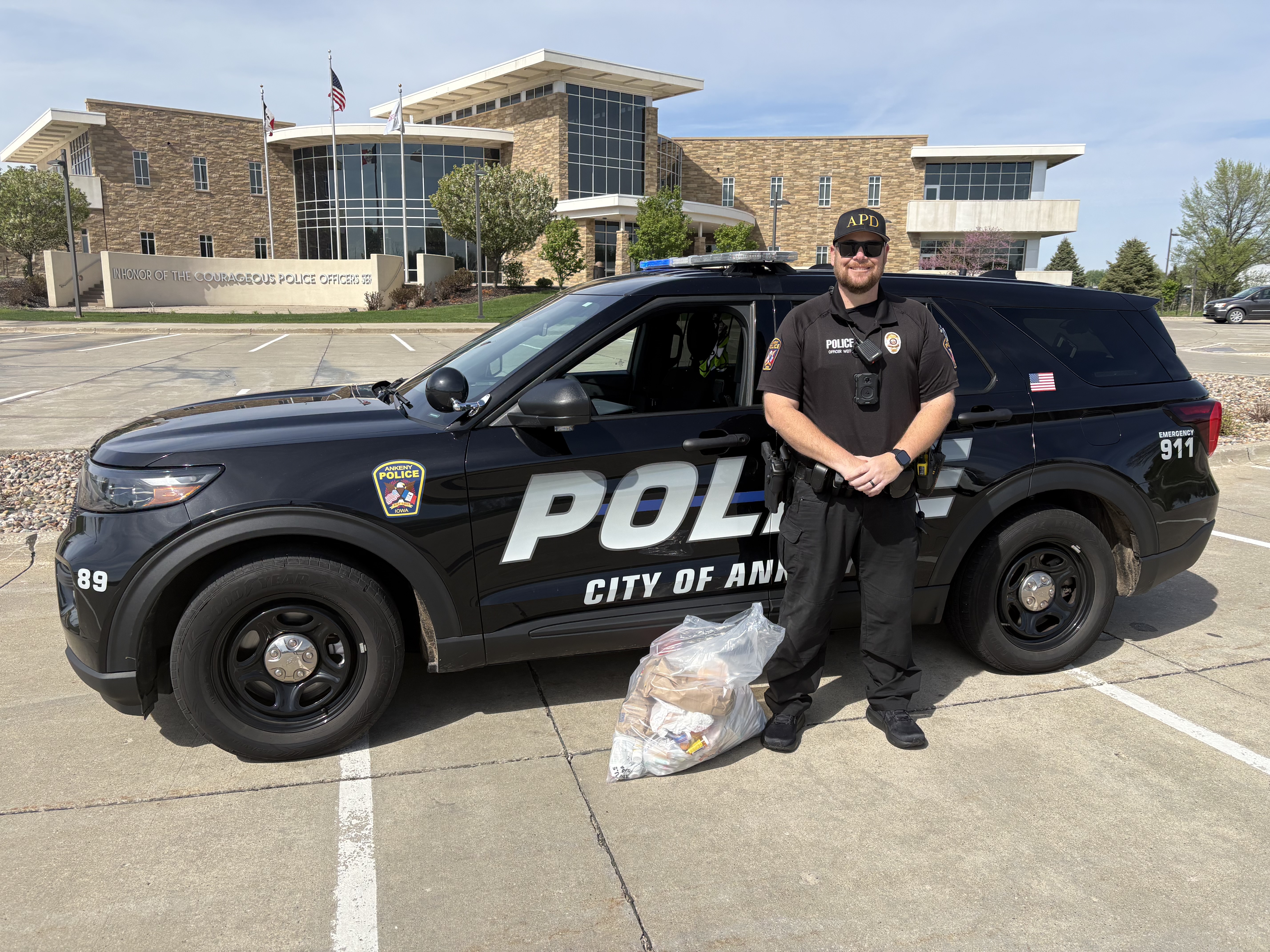 A police officer stands in front of a black vehicle with police markings.