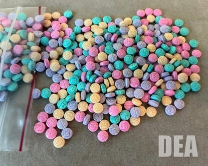 Image of multi-colored pills laying on a table and next to a plastic bag.