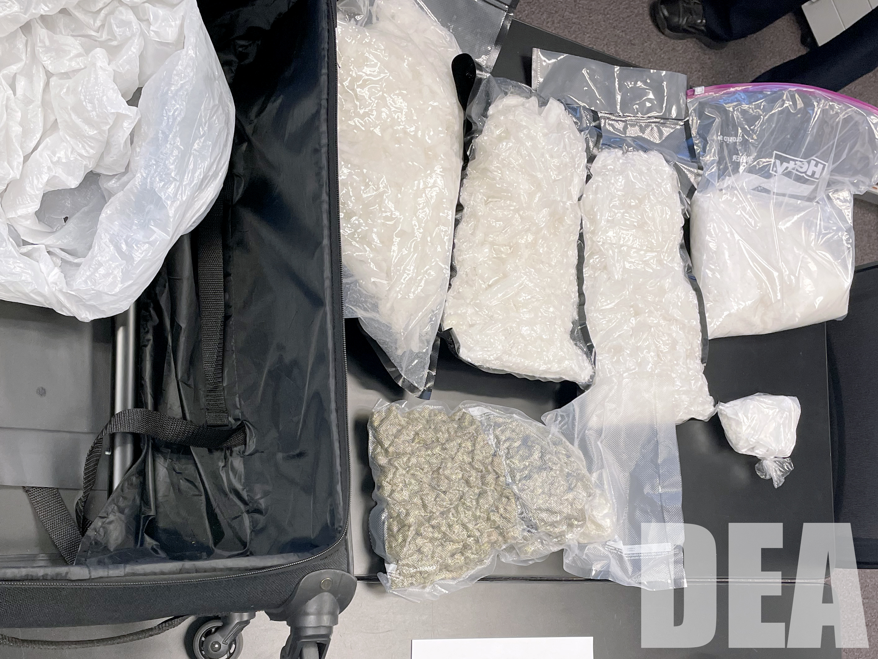 Four plastic bags containing methamphetamine and one bag with marijuana lays on a black table top.