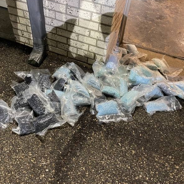 Several clear plastic packages containing blue fentanyl pills lie on the asphalt.