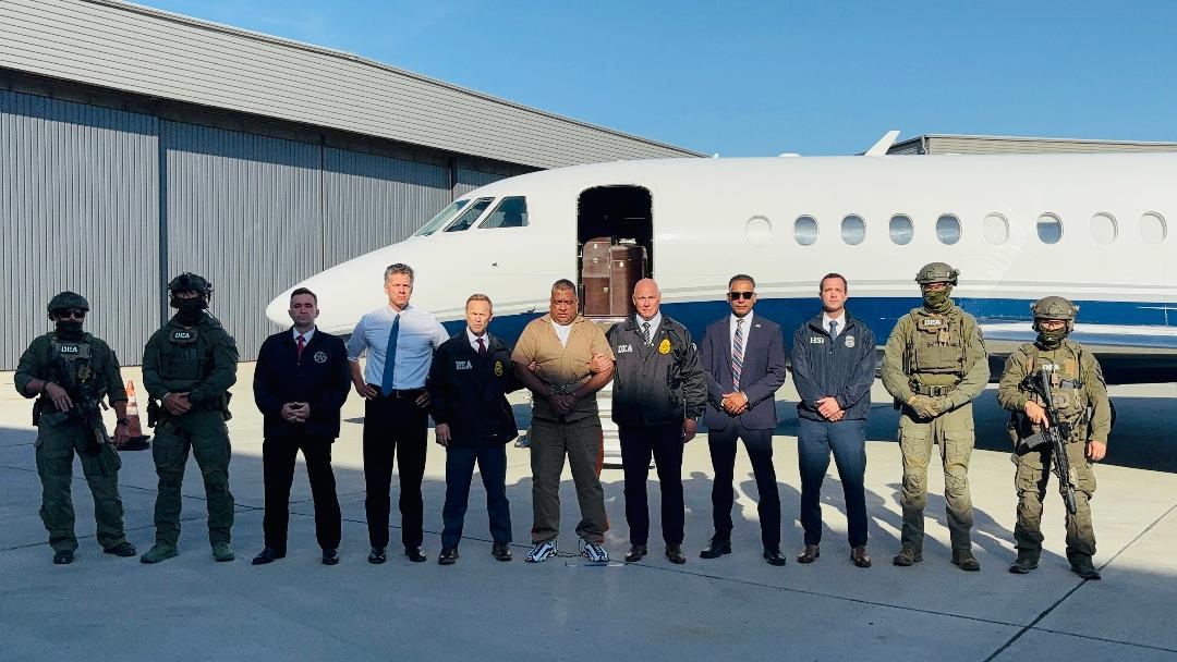 Photo of Rojas (center) flanked by law enforcement after being extradited from Colombia to the United States. Left to right, excluding uniformed agents: U.S. Department of Justice’s Judicial Attaché in Bogotá, Kristopher Jarvis; U.S. Attorney Adam Gordon, Southern District of California; San Diego DEA Special Agent in Charge James Nunnallee; Araña; DEA San Diego Assistant Special Agent in Charge Jacob Galvan; FBI San Diego Assistant Special Agent in Charge Jagdeep Khangura;  Acting Special Agent in Charge H