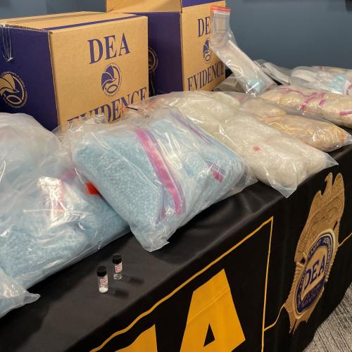 Bags of fentanyl pills on a table top along with other drugs and DEA evidence boxes