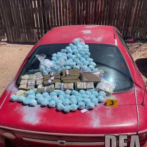 Fentanyl pills and money on the hood of a red car