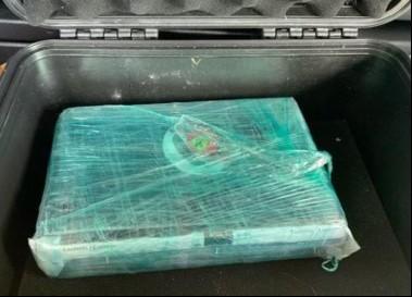 Black suitcase containing a square of seized controlled substance wrapped in green cellophane plastic