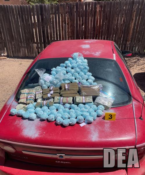 Fentanyl pills and money on the hood of a red car