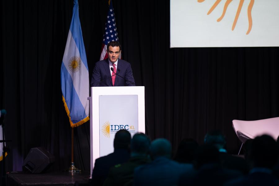 F. Cartwright Weiland, Assistant Secretary of the Bureau of International Narcotics and Law Enforcement Affairs, delivering a presentation at IDEC XL U.S. Drug Enforcement Administration event, with a large logo displayed behind