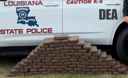 a number of brown wrapped bundles sit in front of a Louisiana State Police SUV