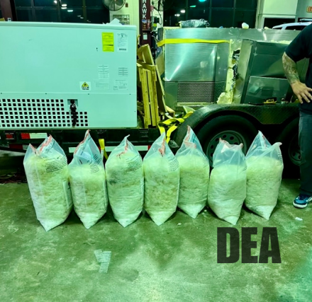 seven plastic bags filled with a white substance sit on a concrete floor of a warehouse